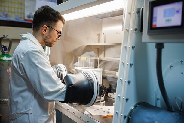 A researcher reaches through the sealed gloves of a laboratory glove box to work with material sealed inside, the barrier keeping it contained.