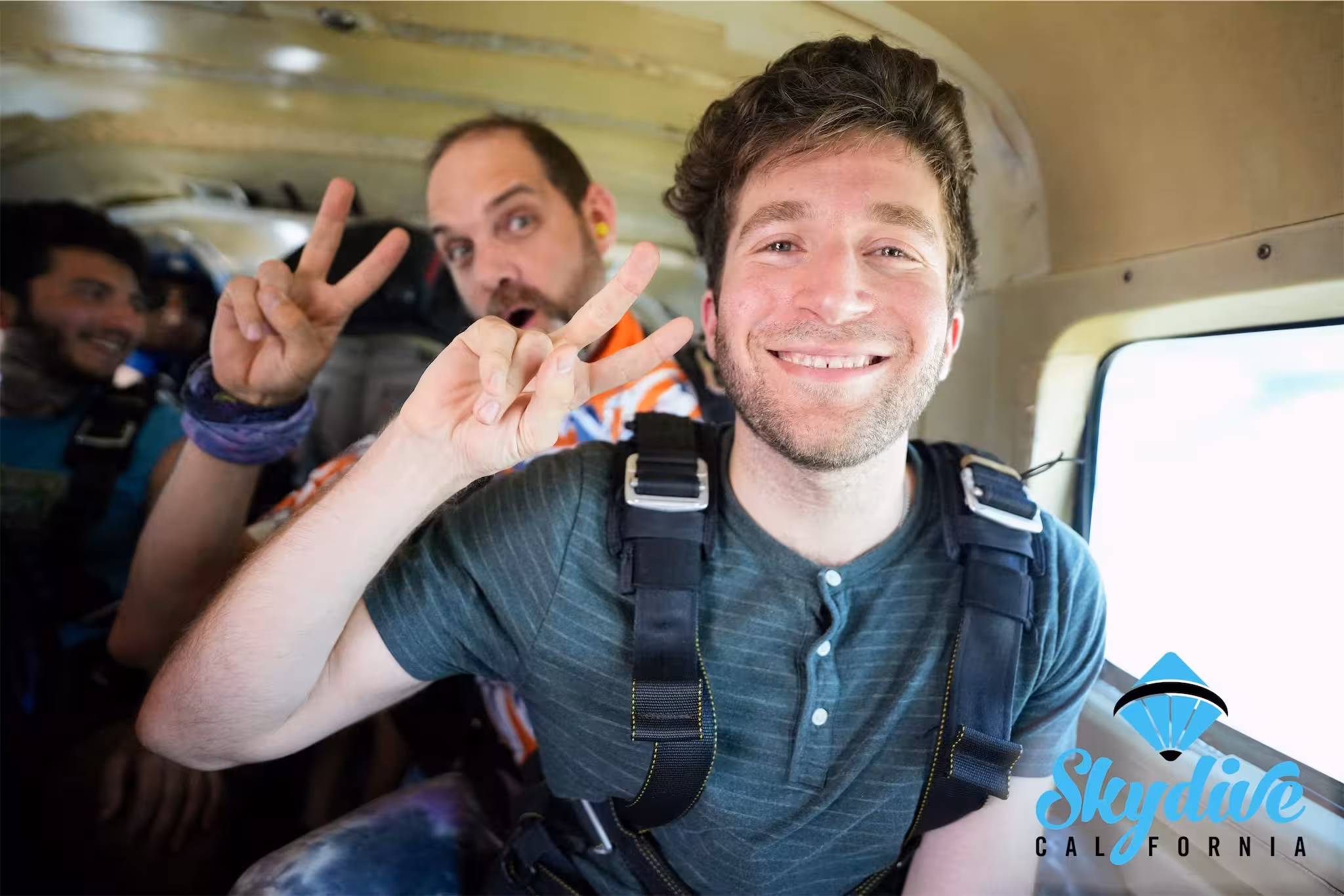 TurnTrout, wearing a skydiving harness inside a small plane, smiles and makes a peace sign at the camera. Another man behind him makes a funny face and also flashes a peace sign.