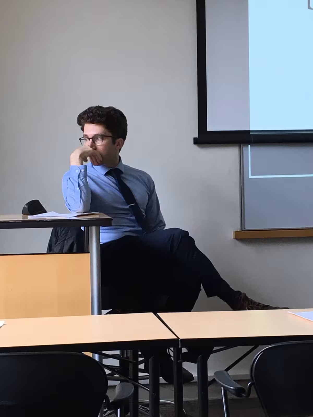 The author, dressed for his thesis defense, sits at a desk with his chin in his hand, looking thoughtfully to the side as he reflects on his alignment research.